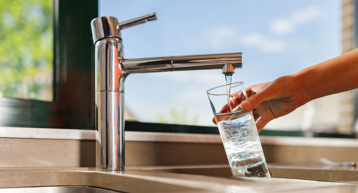 Iemand vult een glas met kraanwater.